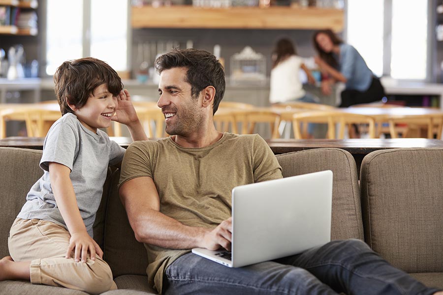 Client Center - Father and Young Son Use a Computer at Their Couch, Mother and Daughter in the Background